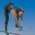 Dynamic shot of an athlete skillfully clearing the pole vault bar under a clear sky.